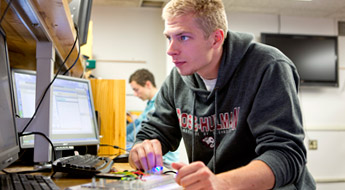 !Male student works at computer station in electrical engineering lab.