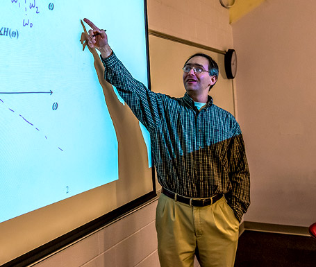 Dr. Simoni points to projected equations on large screen in classroom.