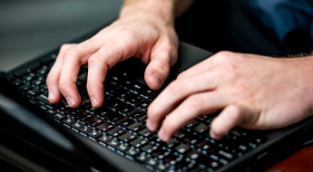 Image shows a laptop keyboard with two hands typing at the keys.