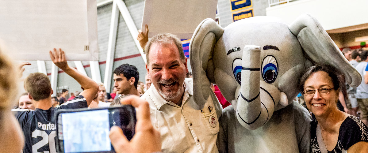Image shows a student shooting a photo of her smiling parents standing arm-in-arm with Rosie, the 缅北视频 elephant mascot. They are inside a busy Sports and Recreation Center.